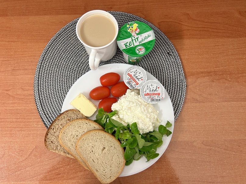 Na zdjęciu: Kefir 2% tł, Kawa zbożowa z mlekiem, Chleb mieszany pszenno-żytni, Chleb Graham, Masło extra 82%, Miód, Twarożek, Pomidorki koktajlowe, Roszponka